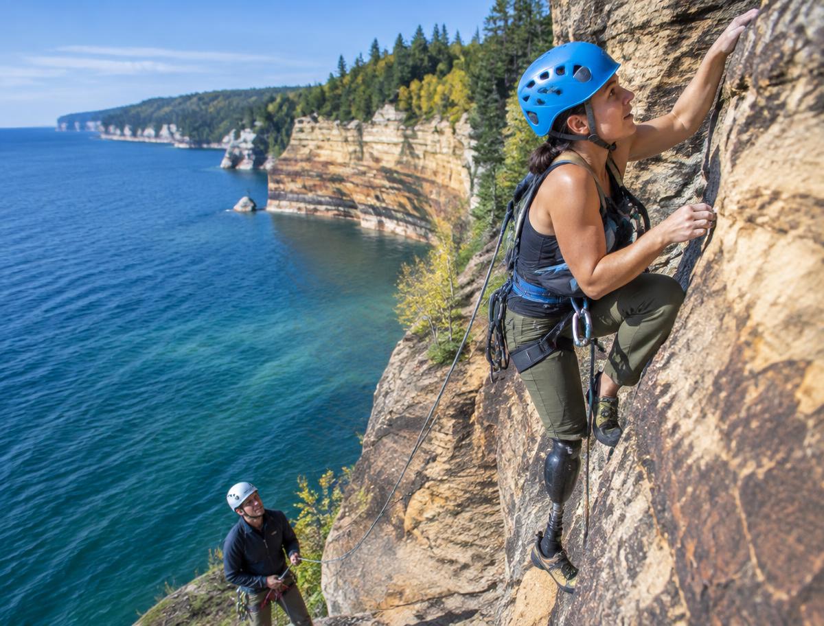 A climber with a prosthetic leg climbing a sandstone cliff above Lake Superior